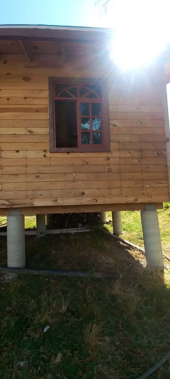Custom wooden house under construction with elevated foundation and window detail.