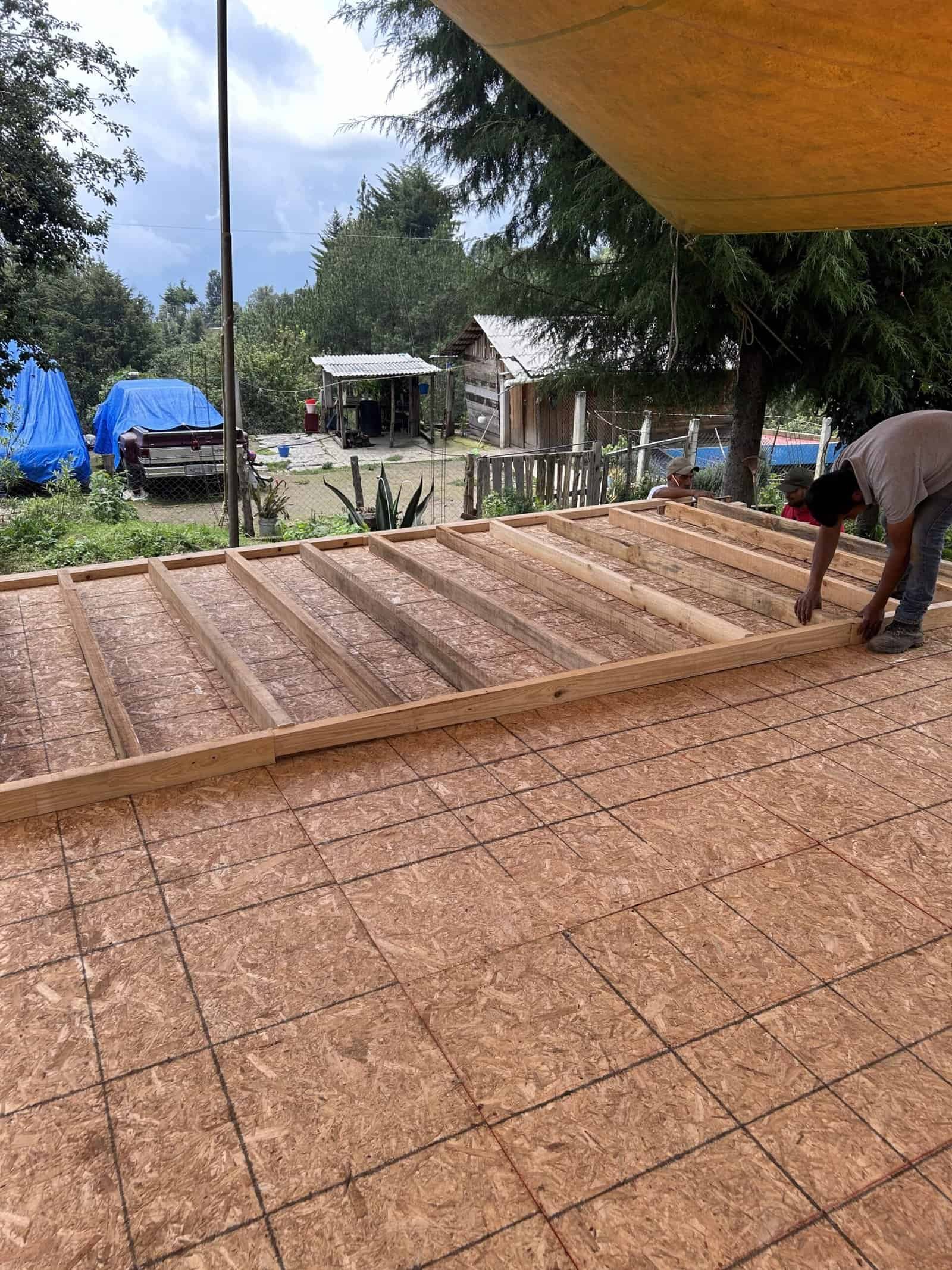 Wooden deck framing under construction with a worker assembling the structure outdoors.