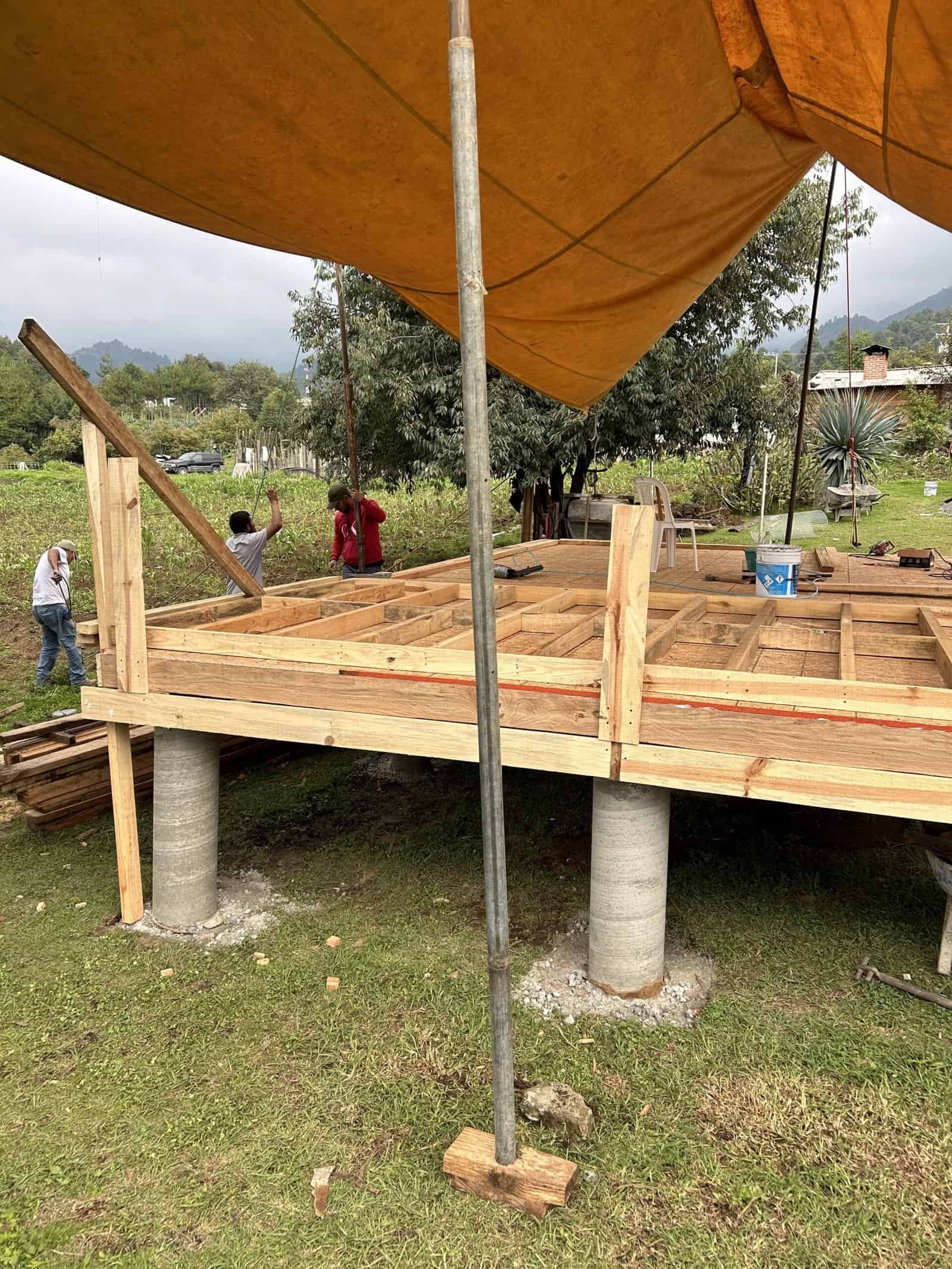 Construction of a house foundation with wooden beams and support pillars in progress.