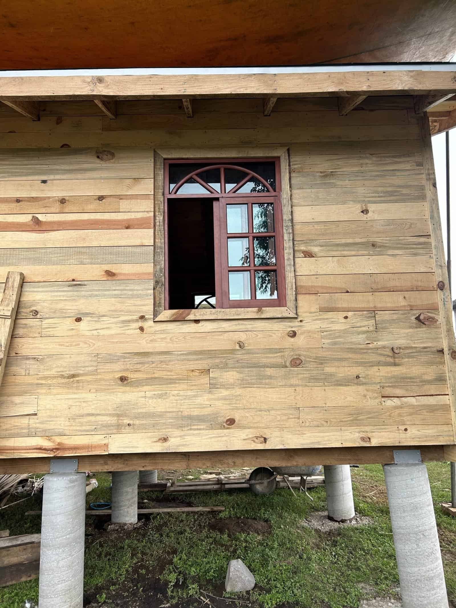 Wooden house under construction with window and elevated foundation.