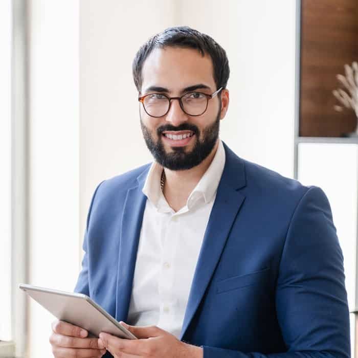 Business professional in a blue suit holding a tablet in an office setting.