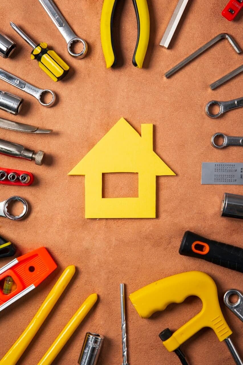 Newly built yellow house-shaped cutout surrounded by various construction tools on a wooden surface.